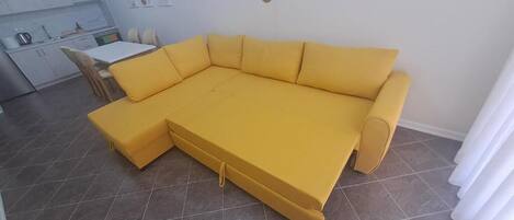 A yellow sectional sofa in a living room with a kitchen area visible in the background.