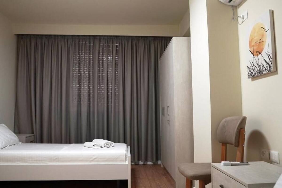 Ein Hotelzimmer mit einem Bett, einem Schreibtisch, einem Stuhl und einem großen Fenster mit Vorhängen.