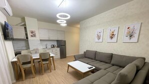 A modern living room with a sectional sofa, a dining table with chairs, and a kitchen area in the background. - Margen Apartments - Tirana City Center (Tirana)