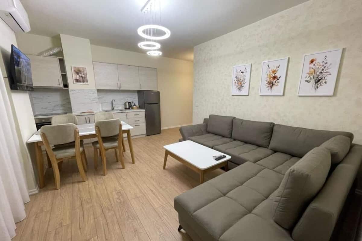 Ein modernes Wohnzimmer mit einem Ecksofa, einem Esstisch mit Stühlen und einer Küchenzeile im Hintergrund.