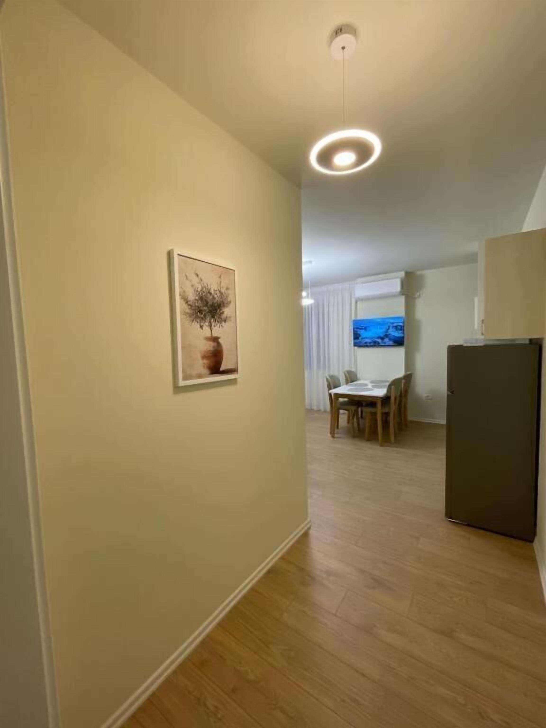 A hallway with a dining area, a TV, and a refrigerator.