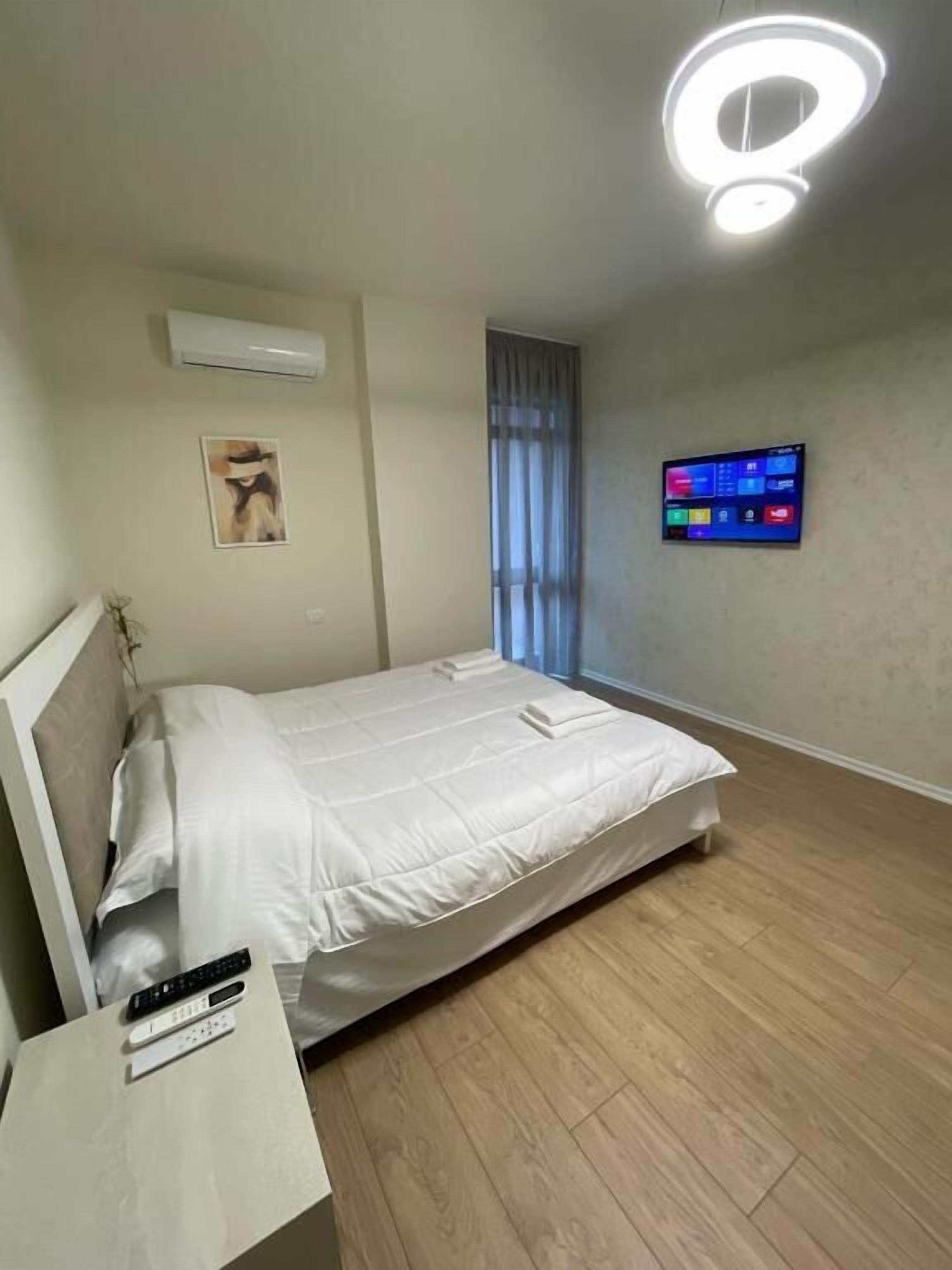 A modern bedroom with a bed, bedside table, and a digital clock on the wall.