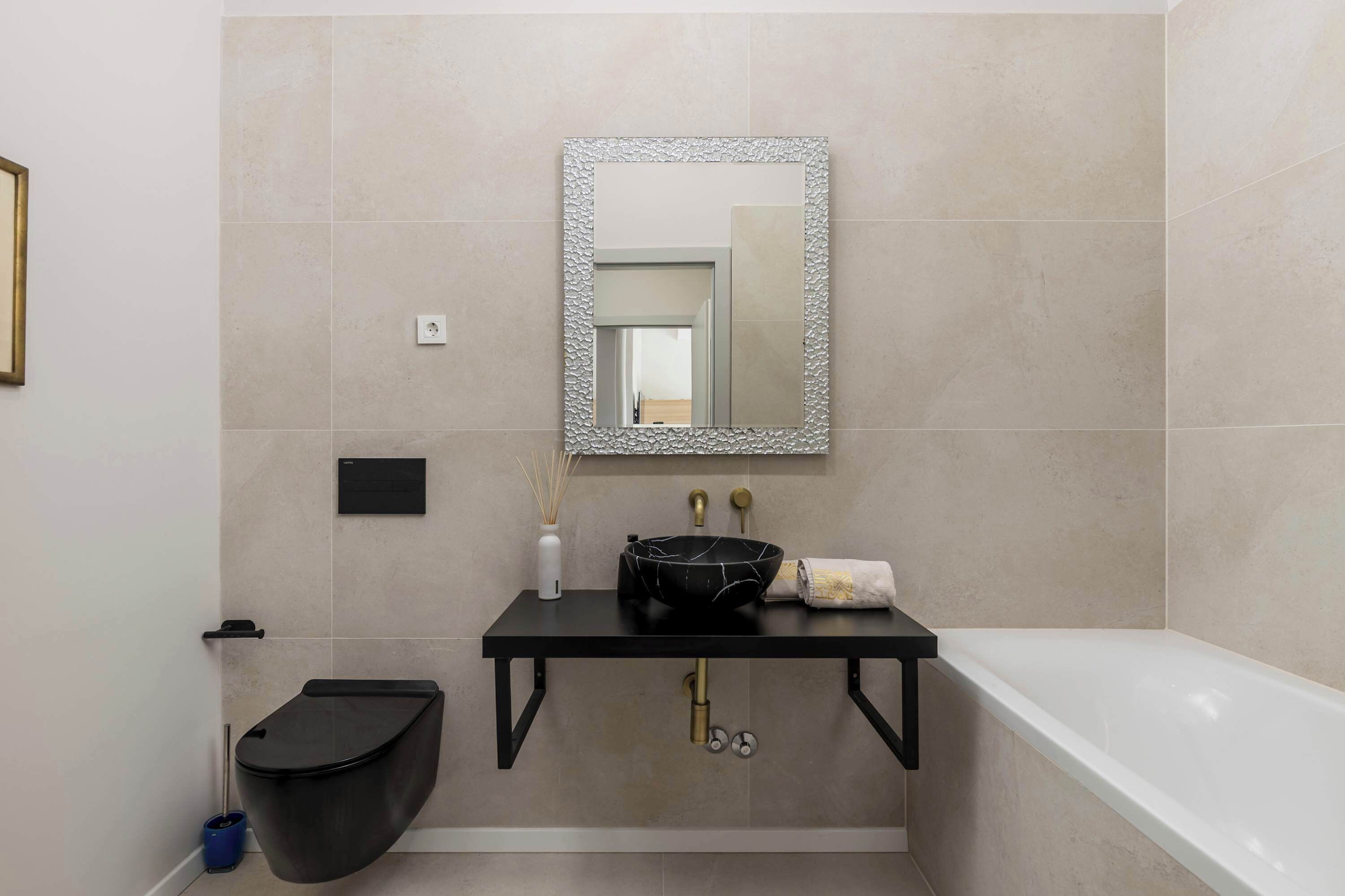 Un bagno con un lavandino nero, uno specchio, un WC e una vasca da bagno.