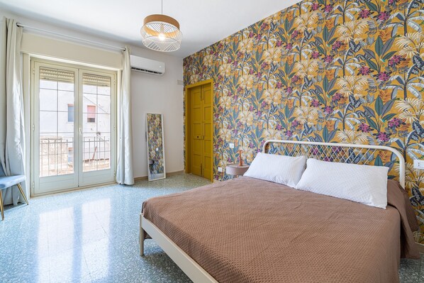 Une chambre à coucher avec un lit, une fenêtre avec des rideaux, une porte et un mur orné d’un motif floral.