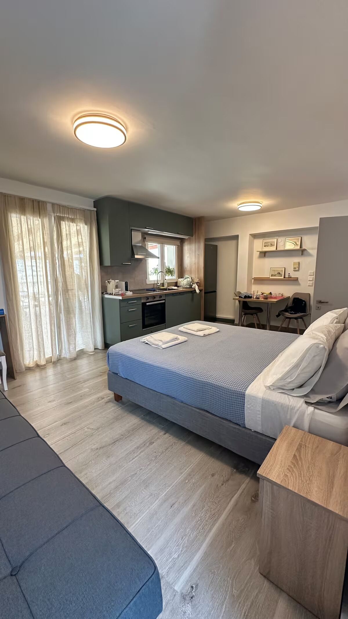 A modern hotel room with a large bed, a desk, a kitchenette, and a seating area.