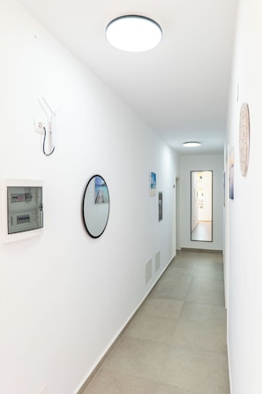 A hallway with white walls, a ceiling light, a framed picture, and a door at the end. - Vila Naço Ksamil (Ksamil)