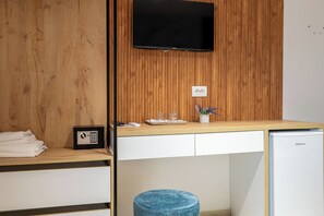 Quarto de hotel com parede de madeira, televisão de tela plana, minibar, um banquinho pequeno e um refrigerador compacto.