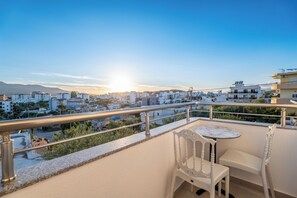 A balcony with a table and chairs, overlooking a cityscape with buildings and a clear sky. - Vila Naço Ksamil (Ksamil)