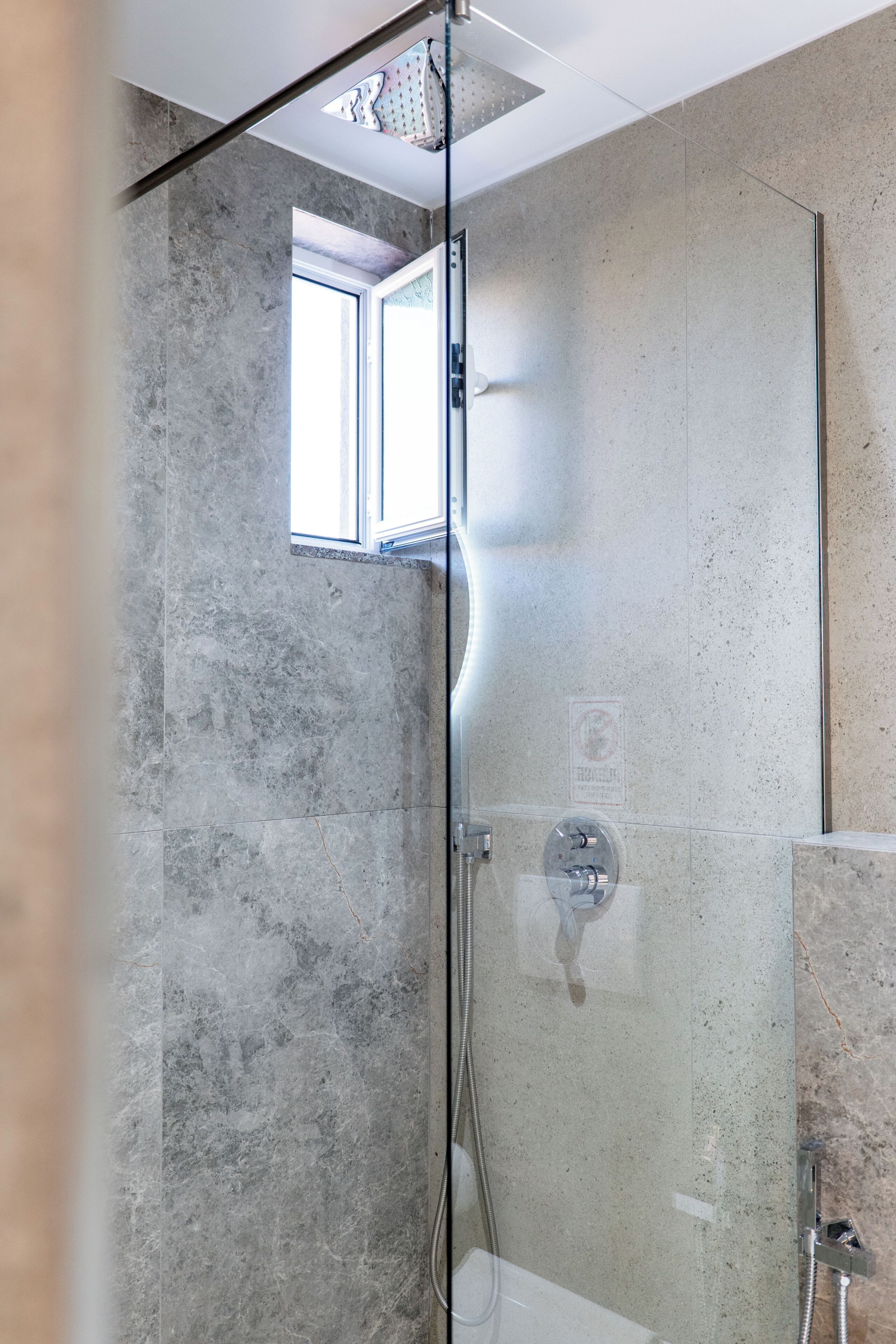 A modern bathroom with a glass-enclosed shower, a window, and a bathtub.