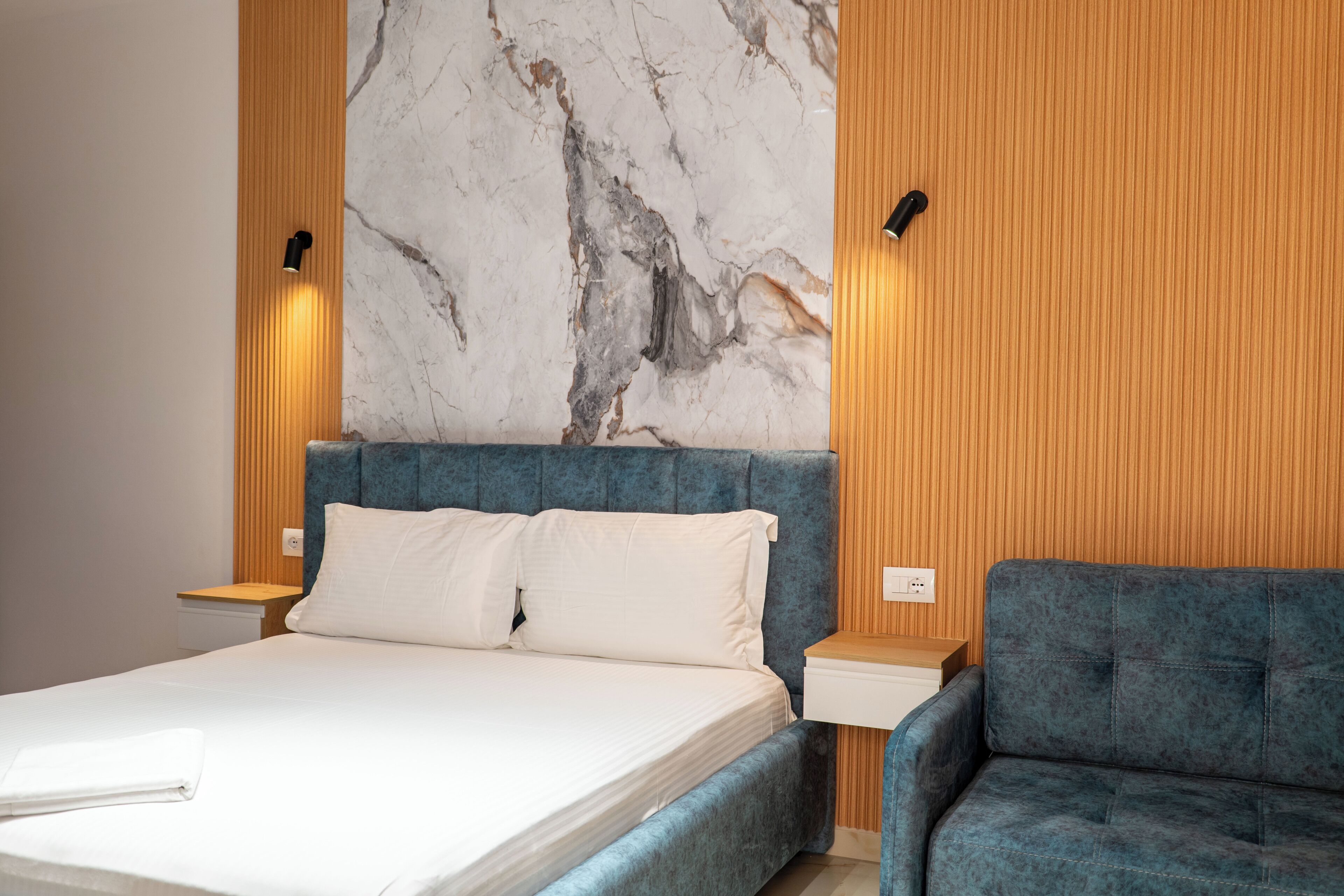 Ein Schlafzimmer mit einem Bett, einem blauen, gepolsterten Sofa, Holzvertäfelung und einer Marmorwand.