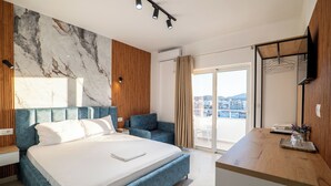 A modern hotel room with a large bed, a desk, a TV, and a balcony with a city view. - Vila Naço Ksamil (Ksamil)