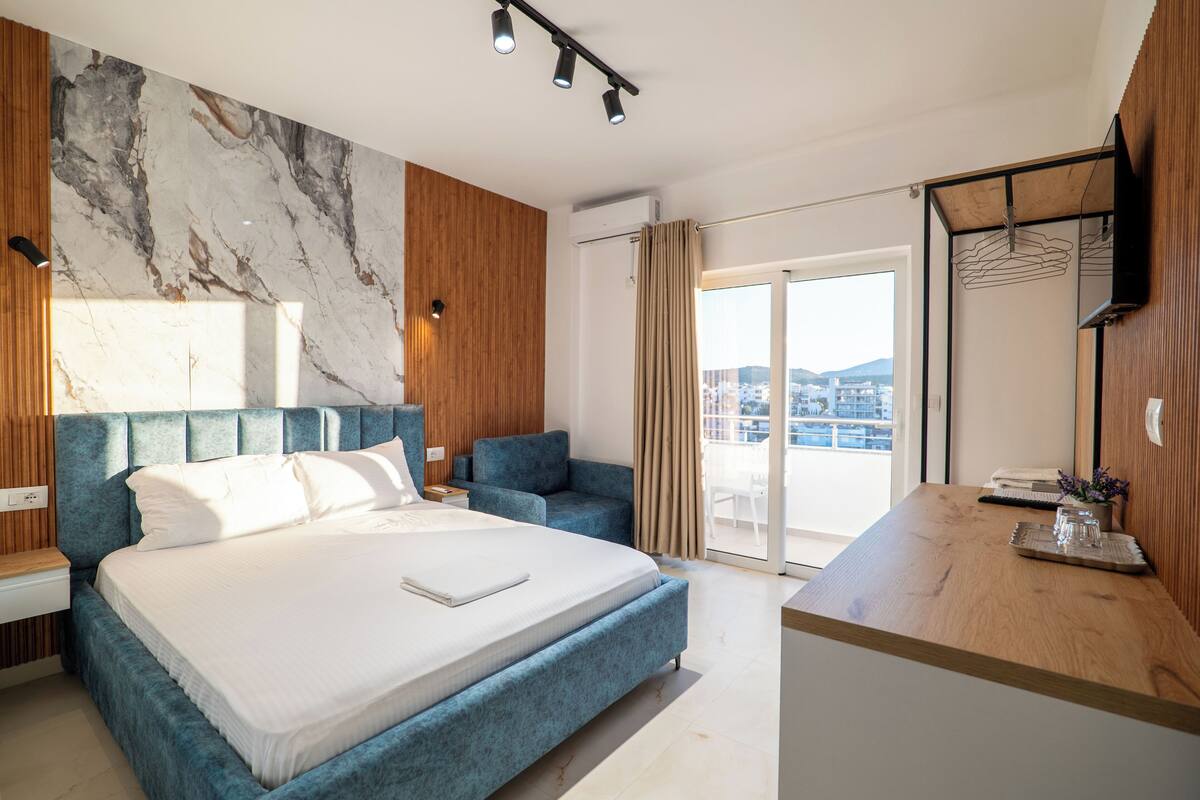 Una habitación de hotel moderna con una cama grande, un escritorio, un televisor y un balcón con vistas a la ciudad.