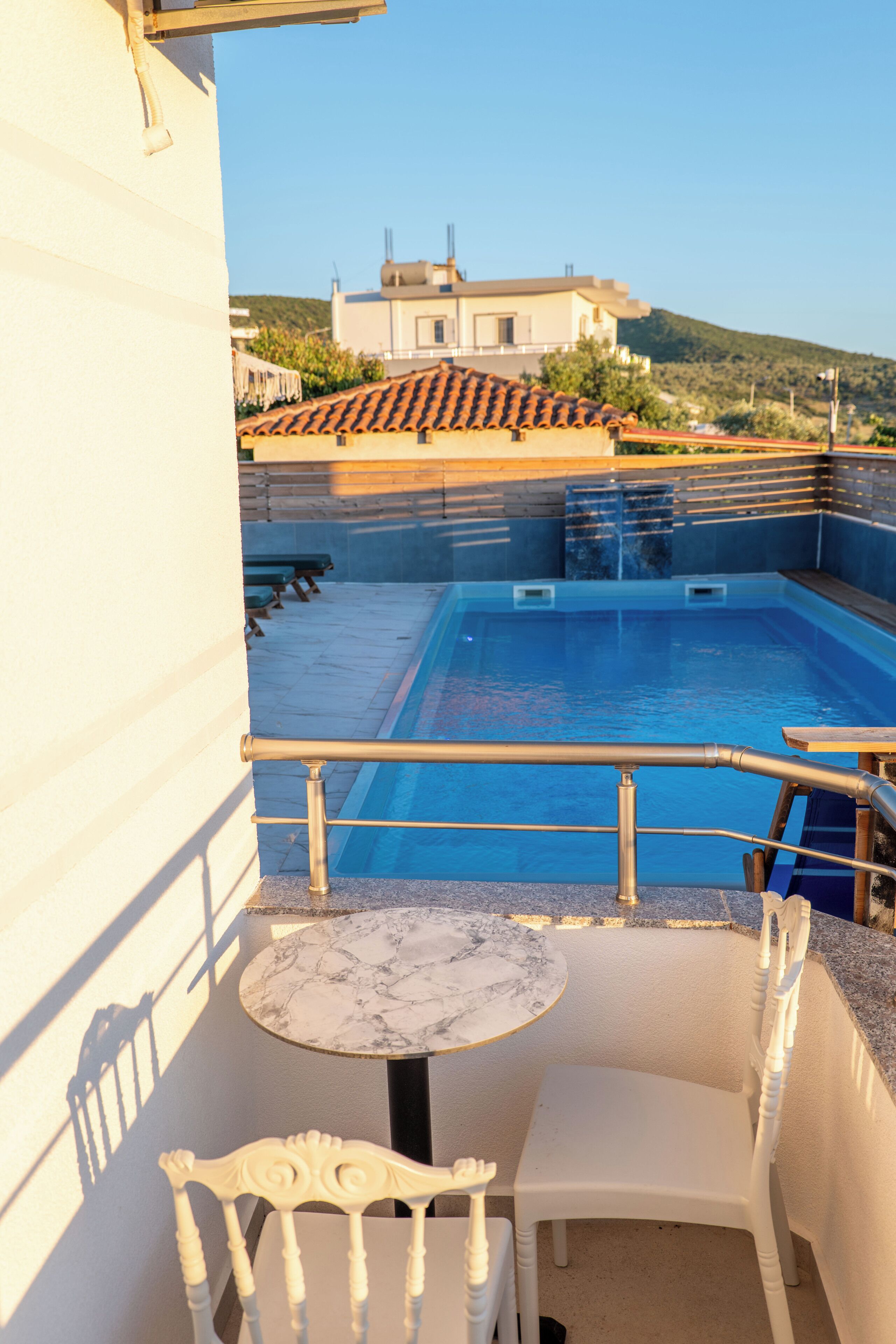 A poolside area with a table and chairs, a view of a building in the background, and a clear sky.