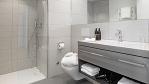 A modern bathroom with a glass-enclosed shower, a toilet, a vanity with a mirror, and a towel rack.