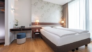 A hotel room with a large bed, a desk with a lamp, a small table, and a chair.