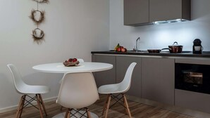 Una cocina moderna con armarios blancos, una mesa redonda con dos sillas blancas y un frutero sobre la mesa.