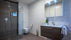 Un baño moderno con ducha envuelta en vidrio, inodoro, tocador con espejo y una planta en maceta.