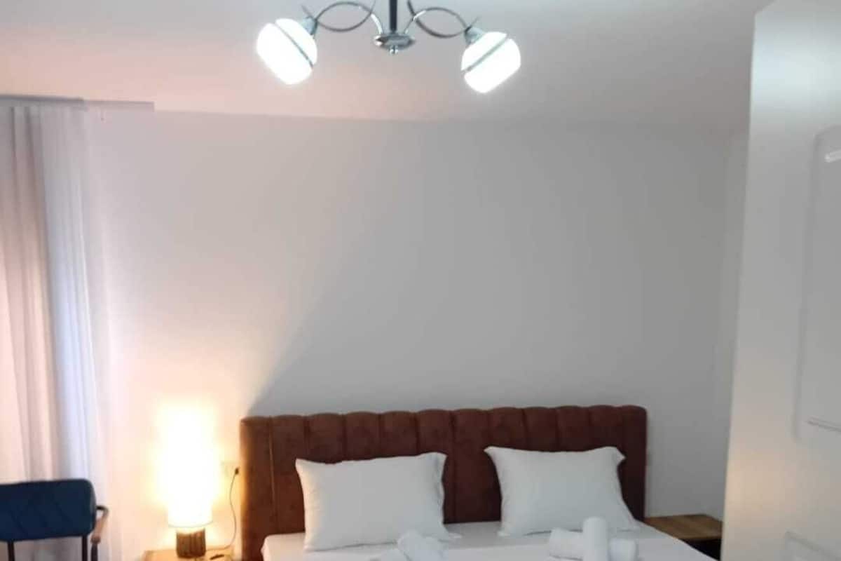 Una habitación de hotel con cama, una silla, una mesita de noche y una lámpara en el techo.