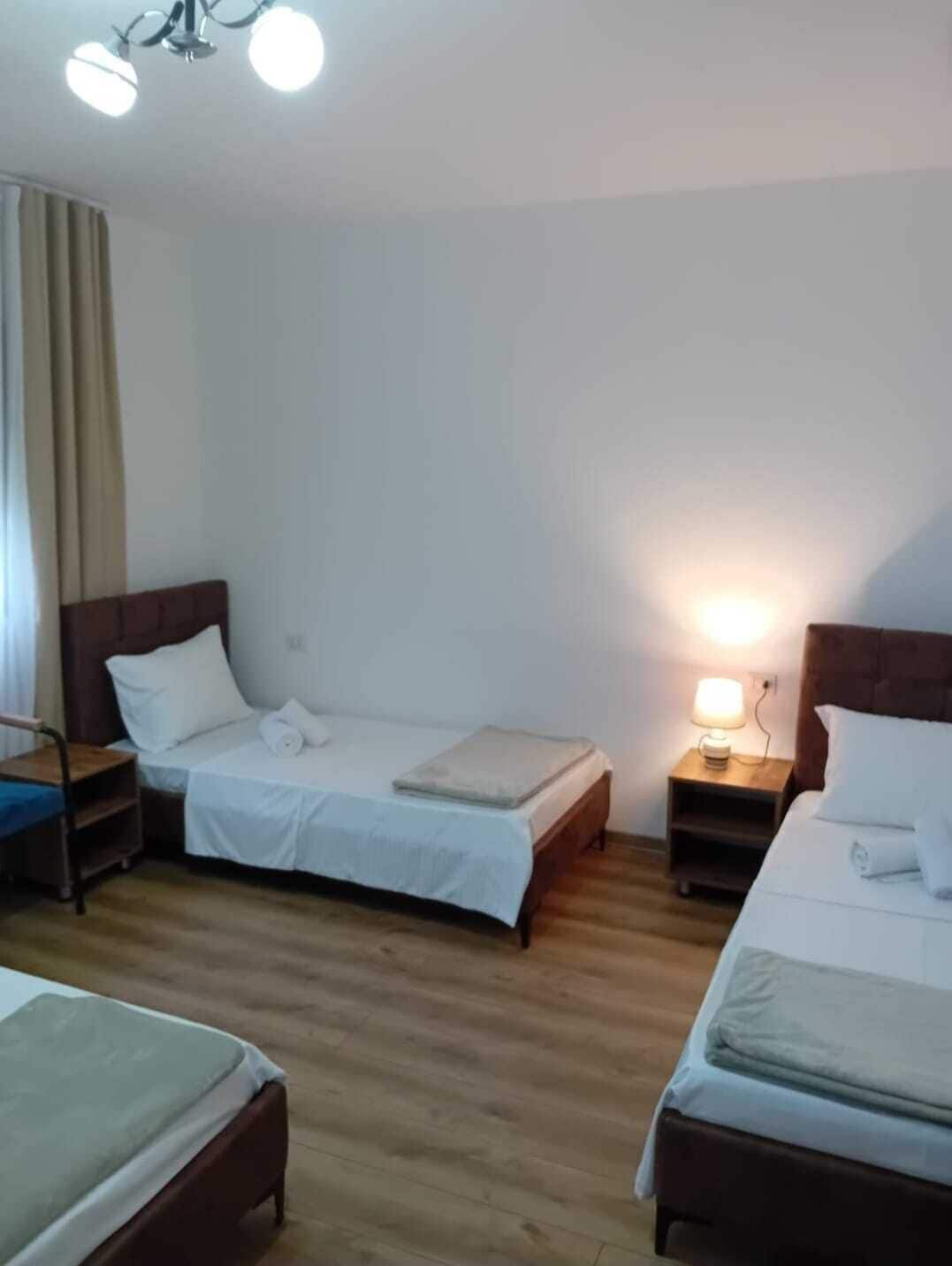 A hotel room with two single beds, a wooden floor, and a ceiling light fixture.