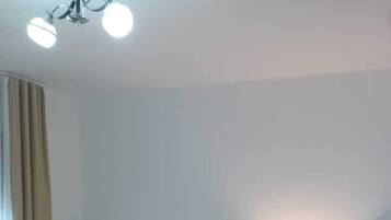 A hotel room with two single beds, a wooden floor, and a ceiling light fixture.