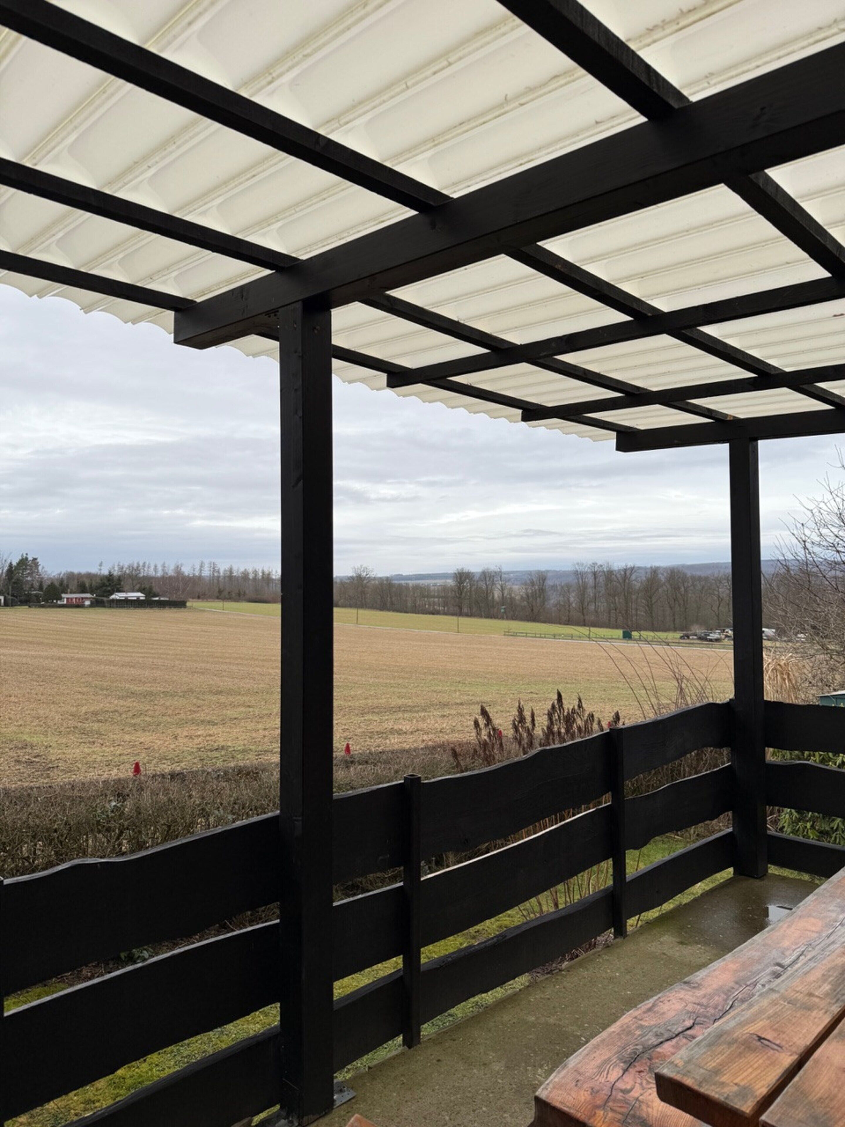 A covered outdoor area with a wooden bench and a view of a field.