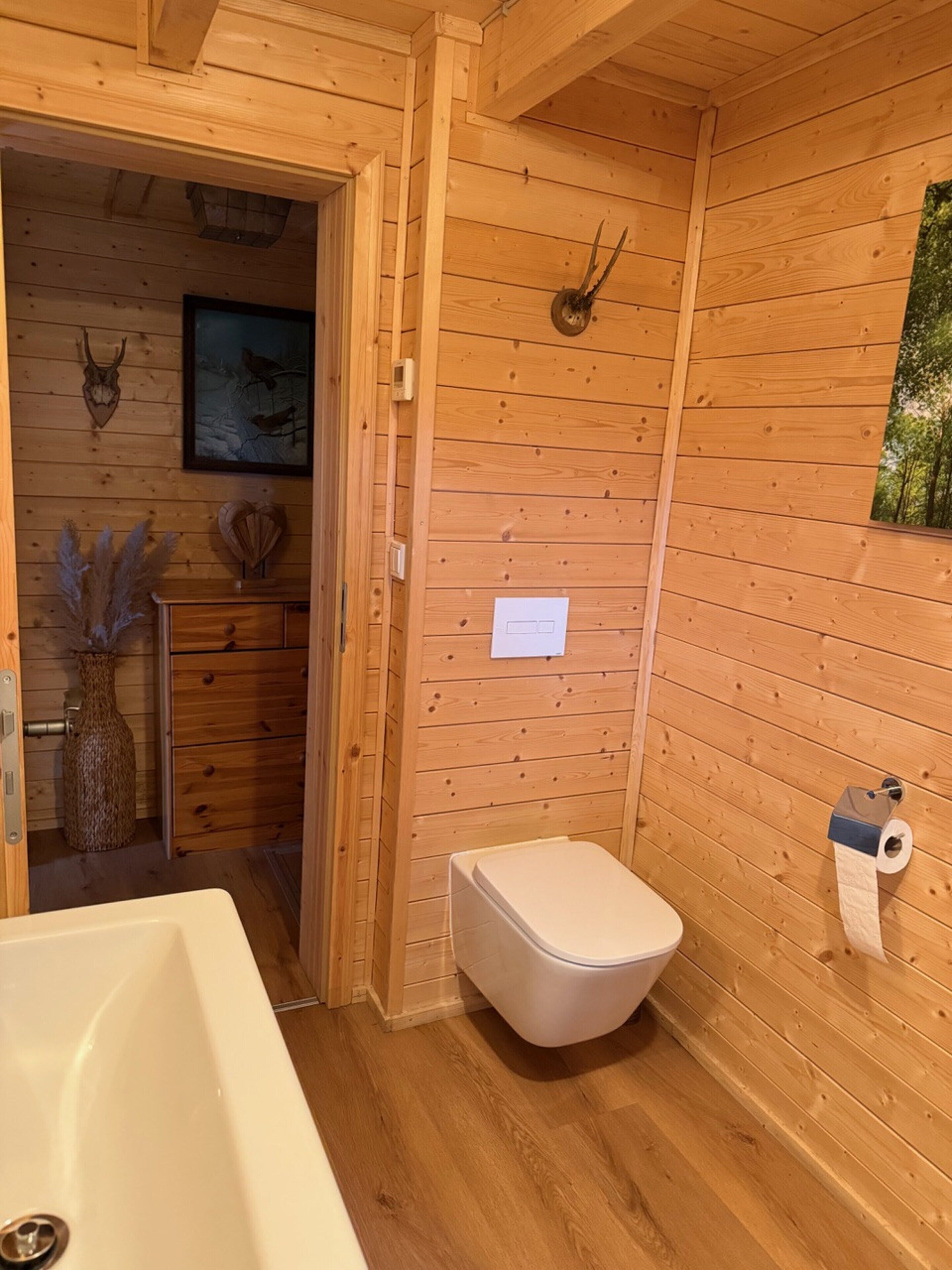 A wooden cabin bathroom with a toilet, sink, and a framed picture on the wall.
