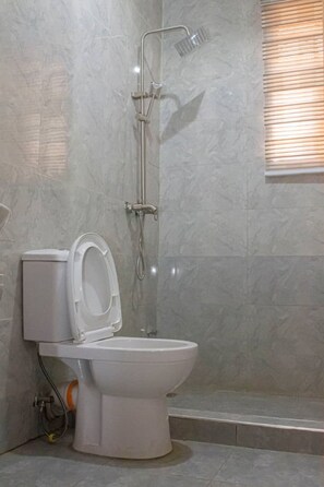 A bathroom with a toilet, shower, and a window with blinds. - Correct Residence & Resort (Abuja)