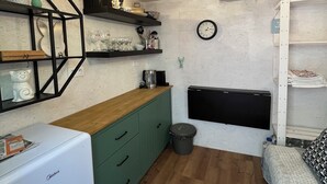 A compact kitchen with wooden flooring, a white refrigerator, green cabinets, and a black countertop. - Tiny house in Posázaví region (Kaliště-Ondřejov)