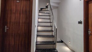 A staircase with a wooden door labeled '103' on the left, a metal railing, and a plain white wall with a light fixture.