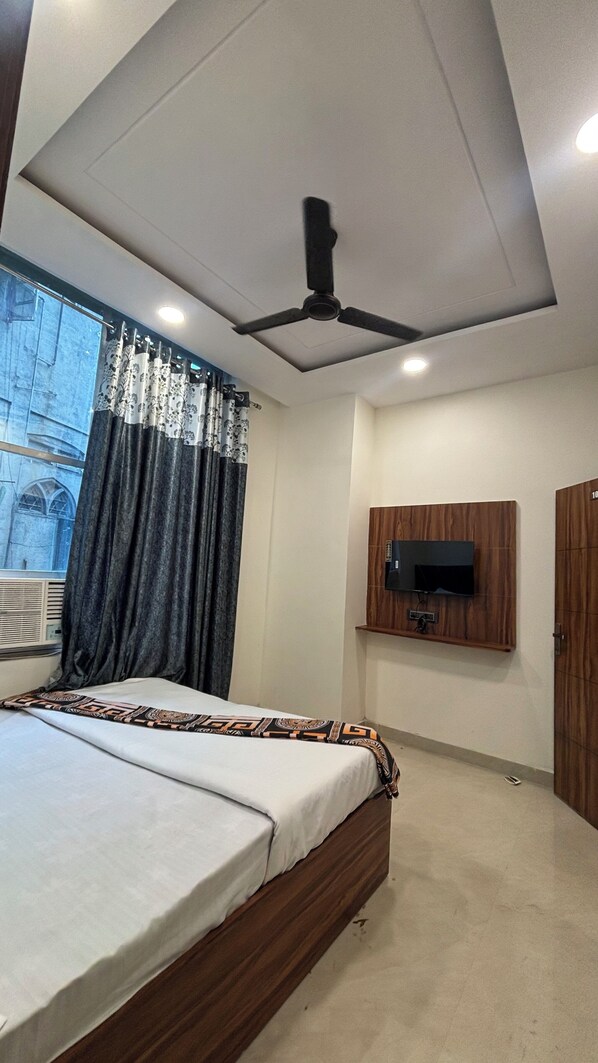 A bedroom with a bed, a ceiling fan, a mounted TV, and a window with curtains.