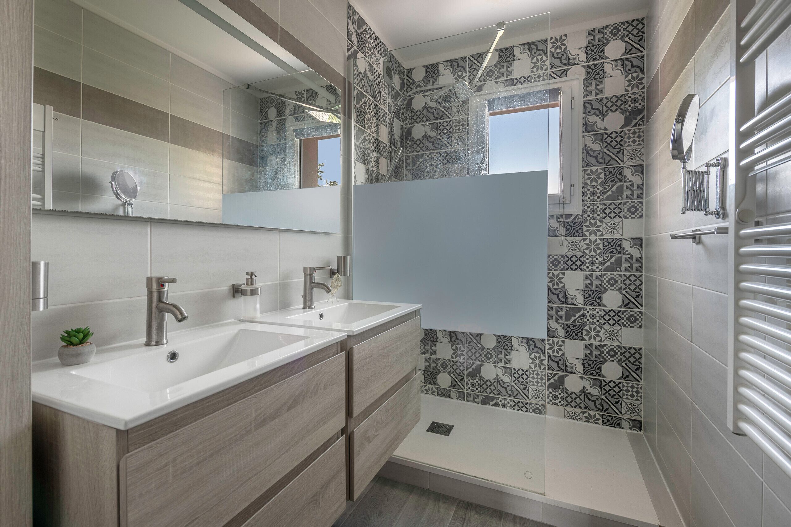 A modern bathroom with two sinks, a large mirror, and patterned tiles.