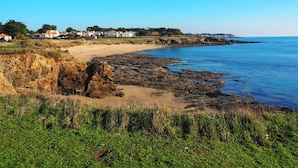 Un paisaje costero con una playa arenosa, un litoral rocoso y casas al fondo.
