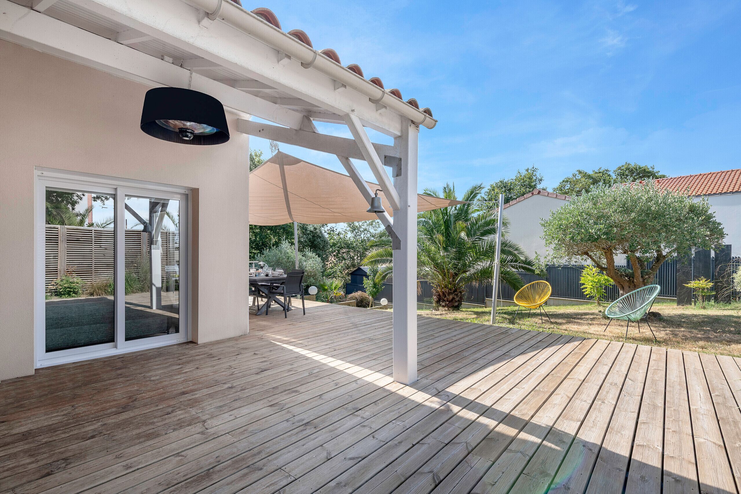 Eine Holzterrasse mit einer Pergola, Sitzgelegenheiten im Freien und Blick auf den Garten.