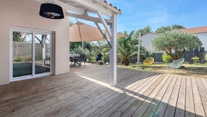 Una terraza de madera con pérgola, mobiliario exterior y vista al jardín trasero.