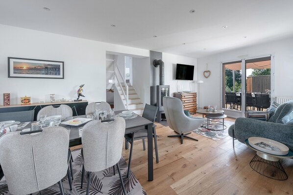 A modern living room with a dining area, a fireplace, and a TV mounted on the wall.