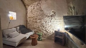 Een gezellige kamer met een stenen muur, een bank, een ronde houten tafel en een flatscreen televisie aan de muur.