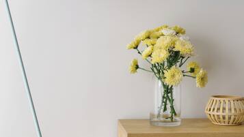 A desk with a vase of yellow flowers, a wooden side table, a woven basket, and a floor lamp.