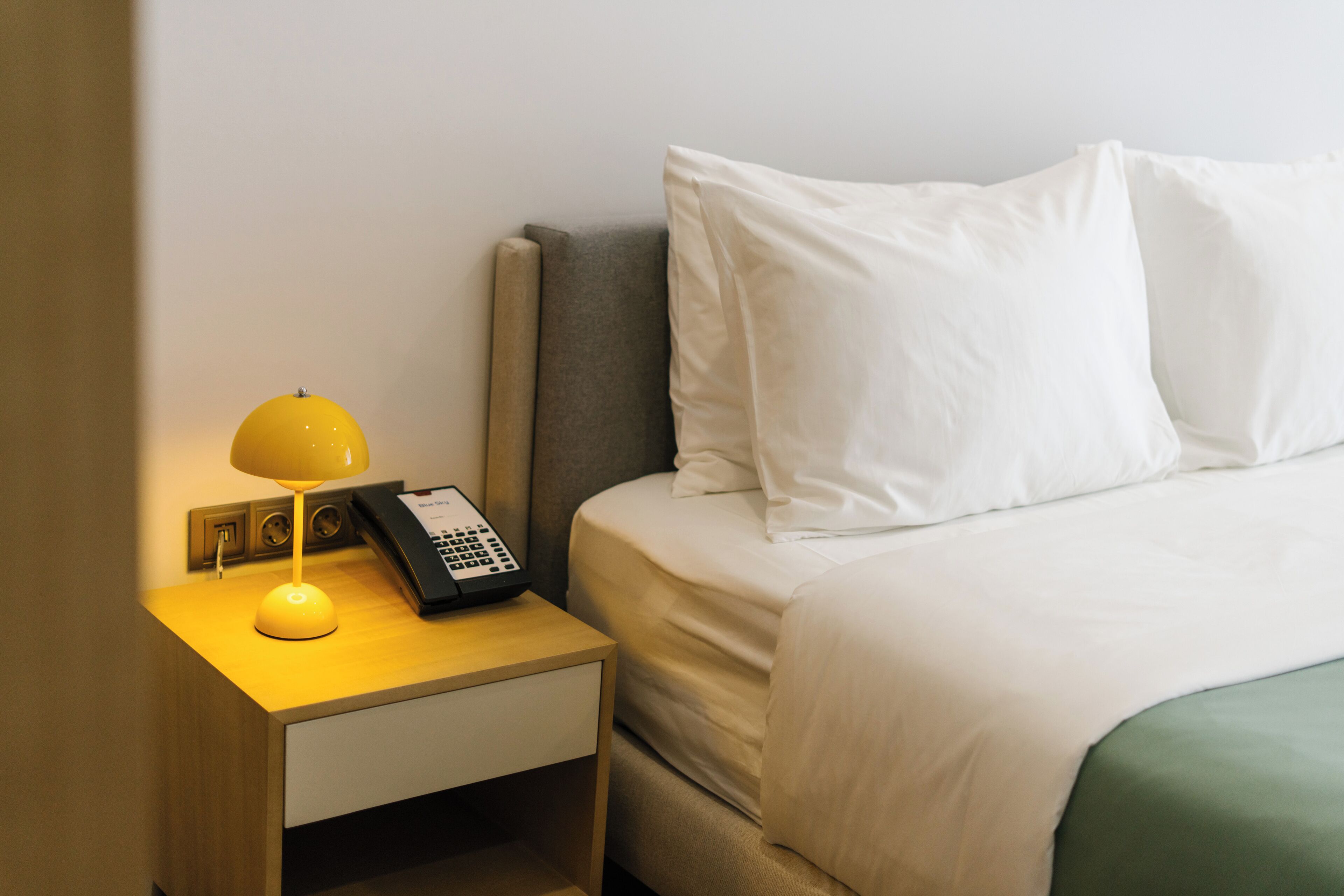 A hotel room with a bed, a bedside table with a lamp, and a telephone.