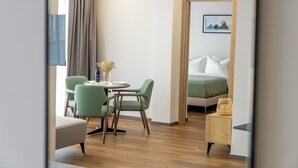 A hotel room with a bed, a dining area with chairs and a table, a small side table, and a window with curtains. - Blue Sky Apart-hotel (Batumi)