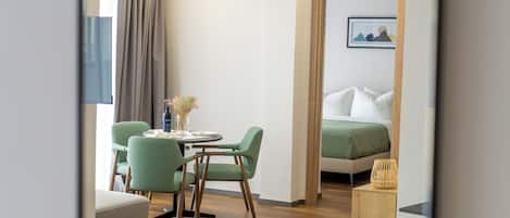 Une chambre d’hôtel comprenant un lit, un coin repas avec des chaises et une table, une petite table d’appoint et une fenêtre avec des rideaux.