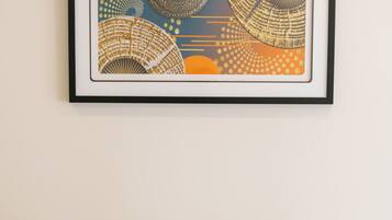 A framed abstract artwork on a wall above a bed with white pillows.