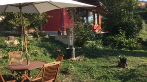 Eine Terrasse im Freien mit einem Holztisch und Stühlen, einem weißen Sonnenschirm und einem roten Gebäude im Hintergrund.