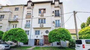 Un immeuble résidentiel à plusieurs étages, doté de balcons, avec un vélo garé à l’extérieur et un fourgon blanc stationné devant.