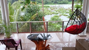 A balcony with a glass table, a wooden chair, and a hanging chair with red cushions. - River Soul Villa/ 3-bedroom house in Riverside (Upputhara)