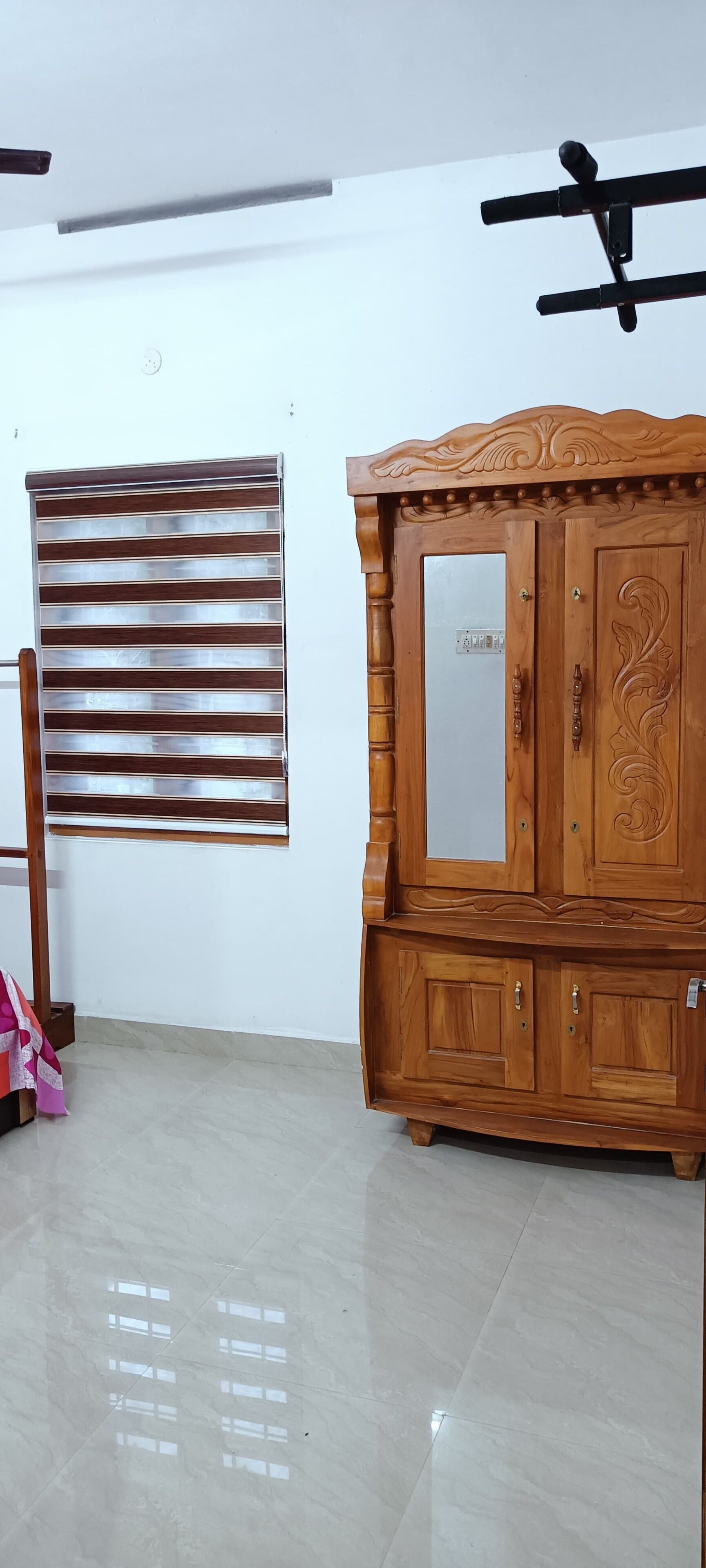 A room with a wooden cabinet, a mirror, and a window with blinds.