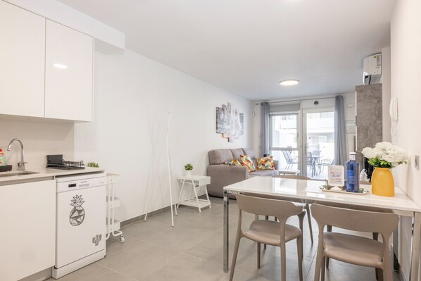A modern kitchen with white cabinets, a dishwasher, and a dining area with a table and chairs.