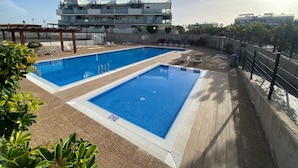 Una piscina con dos zonas separadas, rodeada por un deck de madera y una valla metálica.