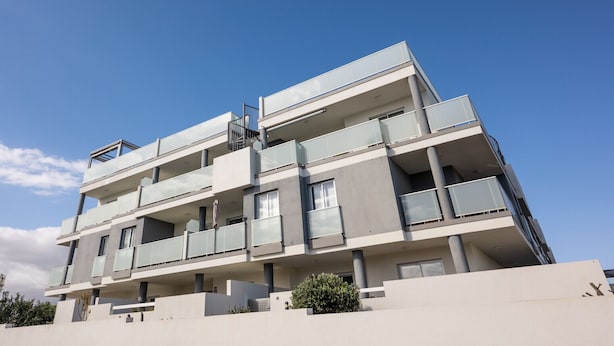 Un edificio residencial de varios pisos con balcones, ventanas amplias y techo plano.