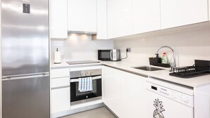 Una cocina moderna con electrodomésticos de acero inoxidable, armarios blancos, horno empotrado, microondas y lavavajillas.