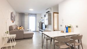 Una sala moderna con un sofá, una mesa de comedor y un televisor. Cuenta con una zona de cocina con refrigerador y microondas.